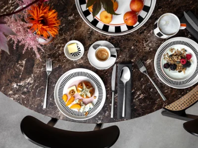Mise en scène de table Memphis extravagante Vue de dessus d'une table en marbre avec des bols de fruits, de café, de céréales et de yaourt de la collection Memphis de Villeroy & Boch, des couverts et des décorations florales.