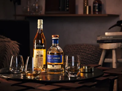 Des verres à whisky écossais sur une table de bar Deux bouteilles de whisky écossais et trois verres Villeroy & Boch sont posés sur une table en bois. En arrière-plan, on peut voir des livres et une figurine décorative.