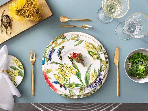 Une table de salle à manger élégante avec une assiette Amazonia Anmut et des couverts de table MetroChic en doré Une table de salle à manger élégante avec une assiette Amazonia Anmut, des couverts de table MetroChic en doré, des verres en cristallin et une figurine en forme de scarabée.