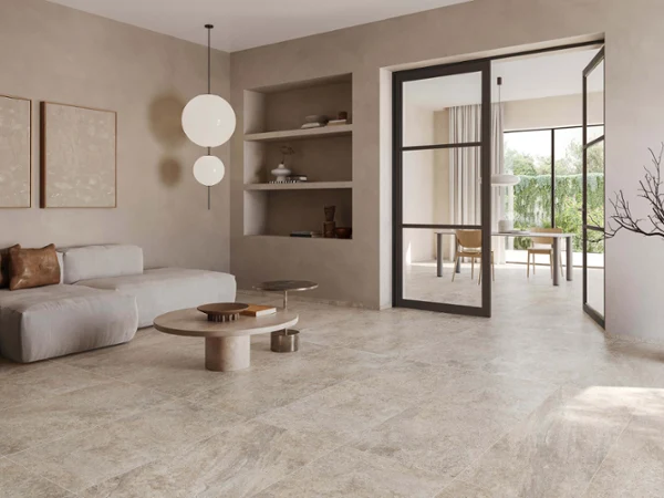 Carreaux de Bourgogne dans un salon clair Salon moderne avec canapé beige, carrelage Bourgogna assorti, luminaires suspendus et porte vitrée donnant sur une pièce adjacente.