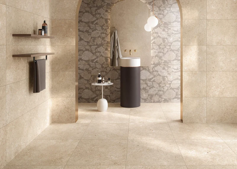 Carreaux Tri.Art dans une salle de bains lumineuse Une salle de bains stylée avec un lavabo cylindrique, des carreaux Tri.Art beiges, une arche à motifs avec des lampes suspendues et des étagères minimalistes.