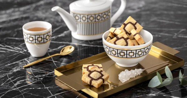 Un service à thé élégant MetroChic avec une théière et une tasse Un élégant service à thé MetroChic avec une théière et une tasse sur un plateau doré, le tout sur une table en marbre.