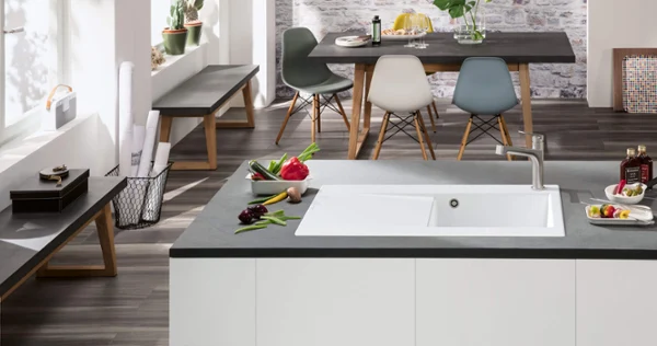 Un intérieur de cuisine moderne avec un plan de travail noir et un coin repas avec des chaises de couleur pastel.