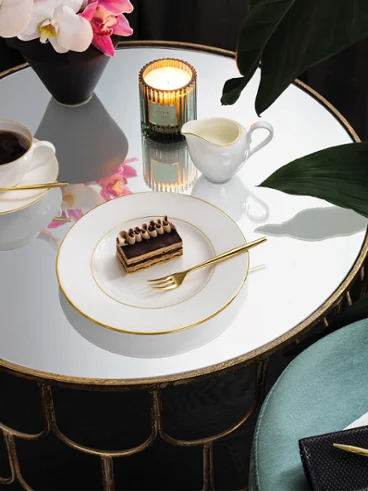 Une table ronde en miroir avec une part de gâteau sur une assiette gracieuse Une table ronde en miroir avec une part de gâteau sur une assiette de grâce, une tasse de café, une bougie, une plante et un tabouret bleu-vert à côté.
