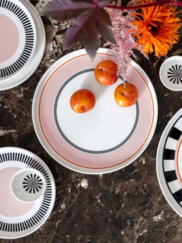 Vue de dessus d'assiettes à motifs représentant trois petites oranges, des fleurs et des feuilles sur une surface structurée sombre.