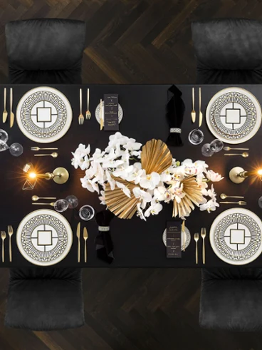 Une table de salle à manger luxueuse avec de la vaisselle MetroChic élégante, des couverts de table et une composition florale sur un sol en bois foncé.