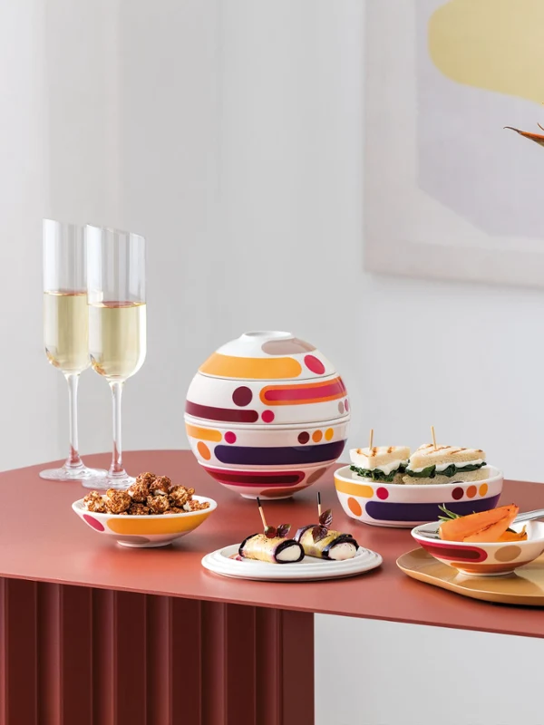 La Boule Miami with Manufacture Blanc Collier Vase in modern arrangement Table moderne avec La Boule Miami, assortiment de snacks, deux coupes de champagne et un vase blanc Manufacture Collier avec des fleurs orange.