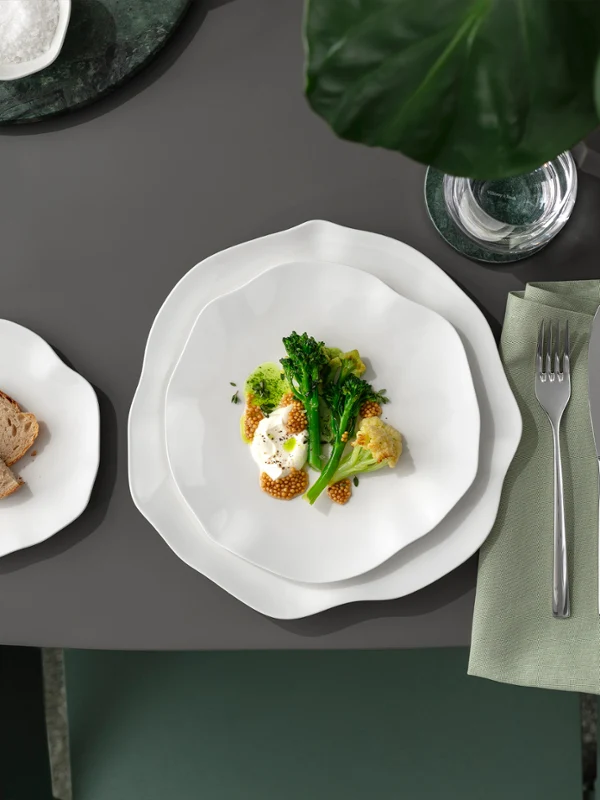 Une assiette Pura avec des légumes et une assiette d'accompagnement sur une table grise Une assiette Pura avec des légumes et un œuf, une assiette d'accompagnement avec du pain et des couverts sur une serviette posée sur une table grise.