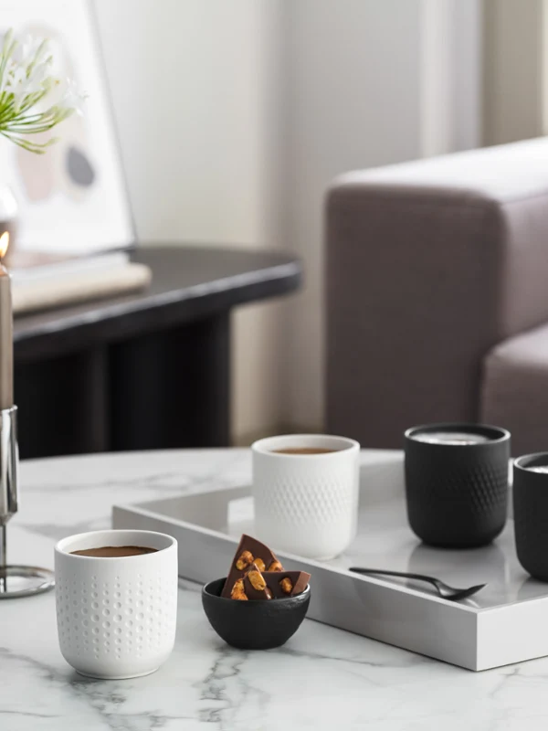 Une table basse élégante dans un salon avec des mugs à café Manufacture Une table basse élégante dans un salon avec des mugs à café Manufacture, des bougies, des vases et un plateau avec des tasses et des en-cas.