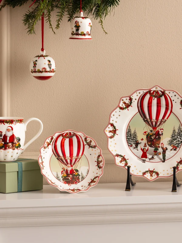 Annual Chistmas edition 2026 collection Des assiettes, tasses et bols en céramique festifs avec des motifs de montgolfières rouges de Villeroy & Boch sont présentés avec des fleurs rouges et des décorations de Noël.