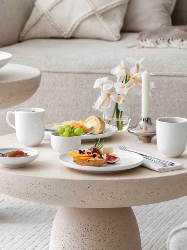 De la vaisselle Afina avec un petit-déjeuner sur une table basse Un petit-déjeuner avec du café, de la confiture et des petits pains garnis sur une table basse beige avec de la vaisselle Afina blanche de Villeroy & Boch.