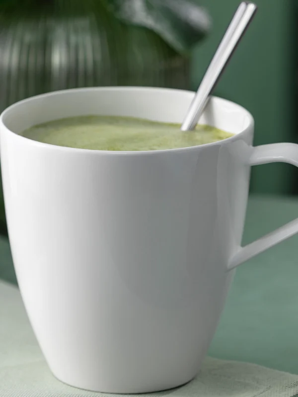 Une tasse blanche Pura Henkelbecher remplie d'une boisson verte. Une tasse blanche Pura Henkelbecher remplie d'une boisson verte et d'une cuillère posée sur une surface claire.