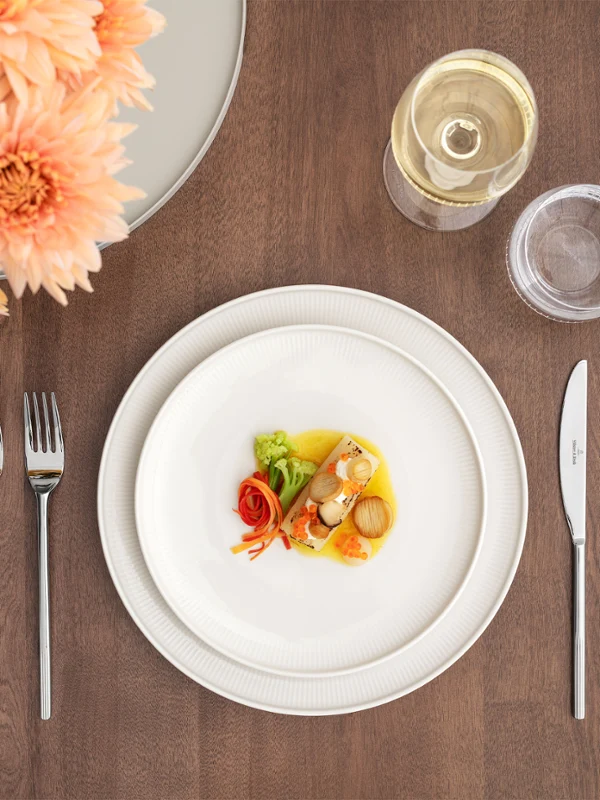 Une table formelle dressée avec la collection Afina, comprenant une petite assiette, un verre à vin, un verre à eau, des couverts, une serviette et un vase à fleurs.
