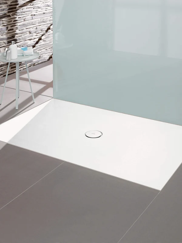 Salle de bains minimaliste avec receveur de douche rectangulaire blanc, paroi en verre et sol carrelé gris.