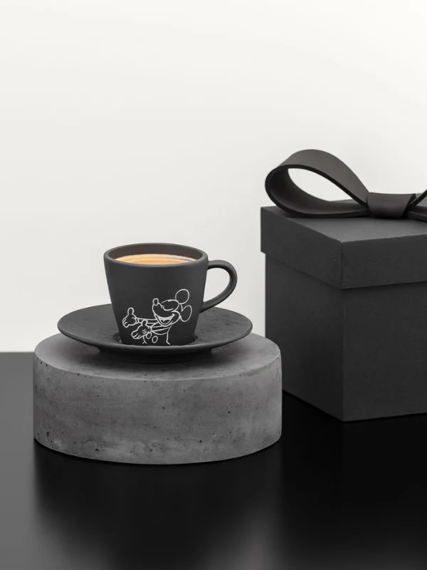 Tasse à café noire et soucoupe sur un socle gris à côté d'un coffret cadeau noir avec un nœud sur une surface noire. Tasse à café noire et soucoupe sur un socle gris à côté d'un coffret cadeau noir avec un nœud sur une surface noire.