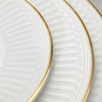 Gros plan sur les détails de la collection Château Septfontaine Trois assiettes en porcelaine blanche posées les unes dans les autres, avec un bord doré et des motifs sophistiqués.
