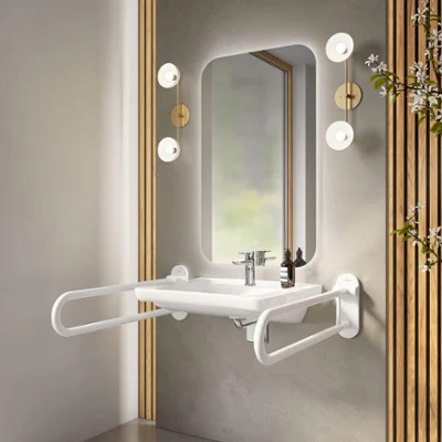 Un lavabo ViCare avec des barres d’appui blanches Un lavabo ViCare avec des poignées rabattables et un miroir avec éclairage d’ambiance sur un mur en crépi gris.