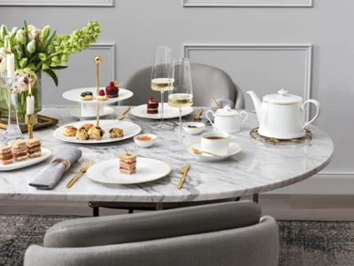 Une table en marbre dressée pour le thé de l'après-midi avec des desserts, des pâtisseries, un service à thé, des flûtes à champagne et une composition florale.