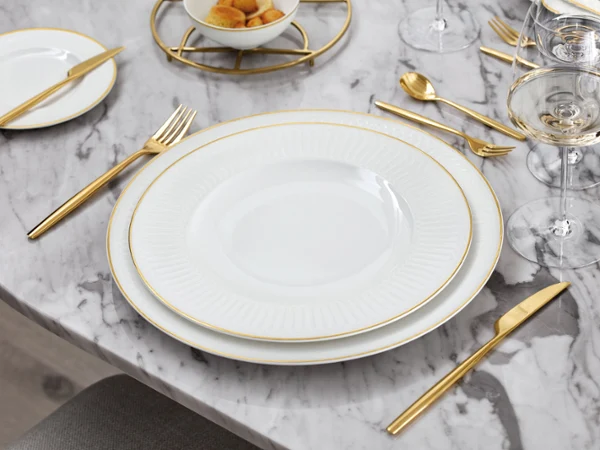 La collection Château Septfontaines dressée sur une table en marbre Un ensemble de vaisselle blanc et doré de Château Septfontaines sur une table en marbre.