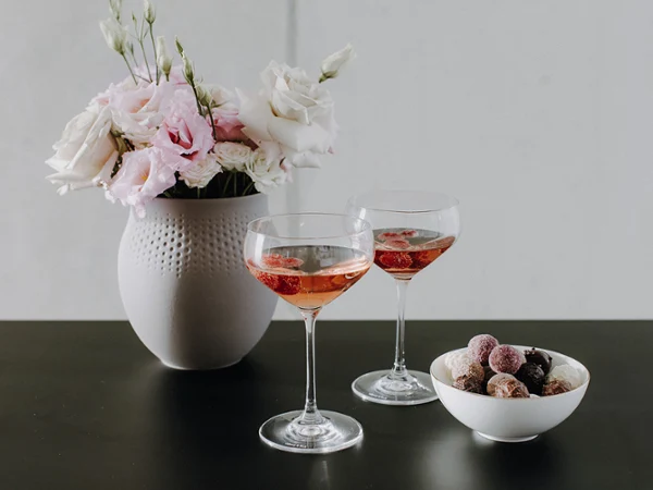 Une carafe en verre et deux verres contenant une boisson sont posés sur une table d'appoint noire. Une carafe en verre et deux verres contenant une boisson sont posés sur une table d'appoint noire à côté d'un lit aux draps blancs.