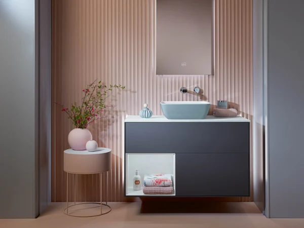 Un meuble sous plan Finion Meuble sous plan Finion bleu foncé de Villeroy & Boch dans une salle de bains rose avec une table basse rose.