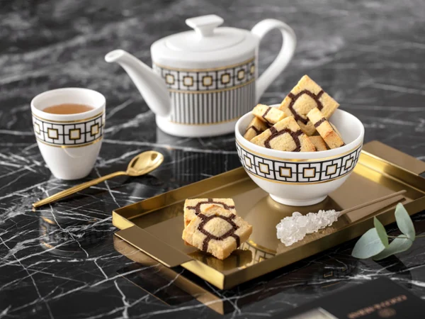 Un service à thé élégant MetroChic avec une théière et une tasse Un élégant service à thé MetroChic avec une théière et une tasse sur un plateau doré, le tout sur une table en marbre.