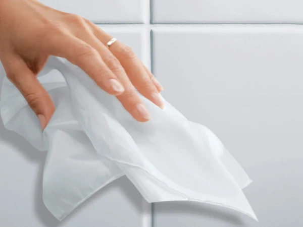 Nettoyage d’un carrelage blanc Une main portant une bague essuie un mur carrelé blanc avec un chiffon blanc.