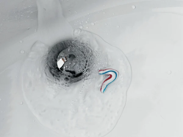 Un lavabo encrassé avec de l’eau qui s’écoule Une petite quantité de dentifrice et d’eau s’écoule via l’évacuation d’un lavabo de salle de bains, formant des bulles autour du cache-bonde.