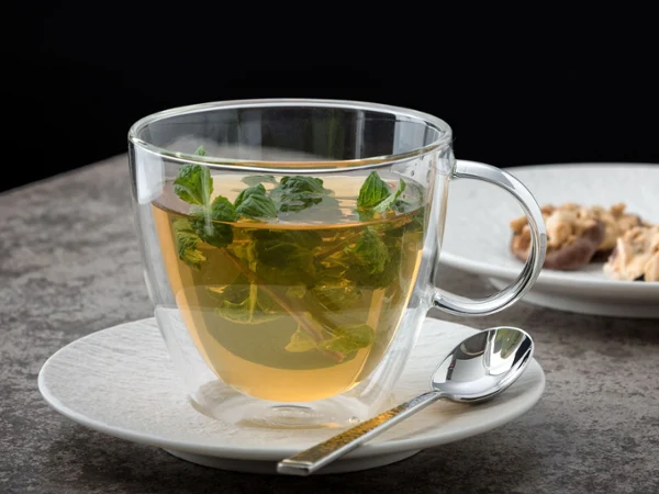 Une tasse Artesano Hot&Cold Beverages avec des feuilles de menthe sur une sous-tasse. Une tasse Artesano Hot&Cold Beverages avec des feuilles de menthe sur une sous-tasse, accompagnée d’une cuillère, sur un fond sombre.
