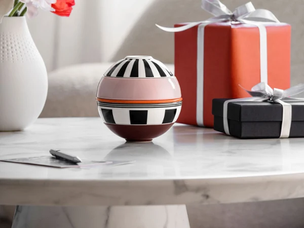 La petite Boule Memphis de Villeroy & Boch et deux cadeaux emballés sont posés sur une table en marbre, avec un vase de fleurs en arrière-plan.