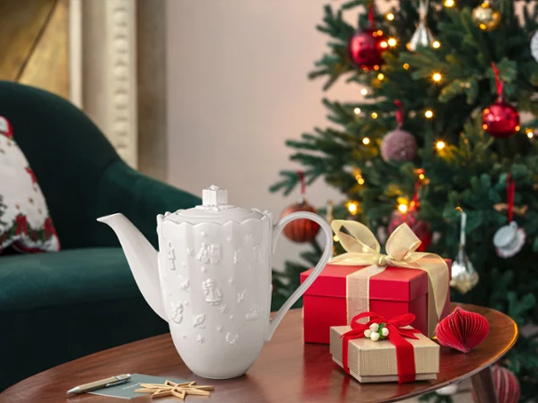 Toys Delight Royal Classic tea and coffee jug Two wrapped gifts and a white Toys Delight Royal Classic ceramic jug stand on a wooden table next to a decorated Christmas tree.