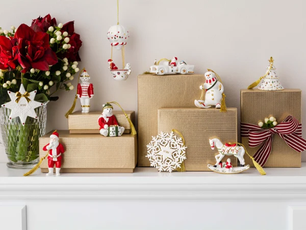 Plusieurs paquets cadeaux, des décorations de Noël et un vase rempli de fleurs rouges sont disposés sur une cheminée blanche.
