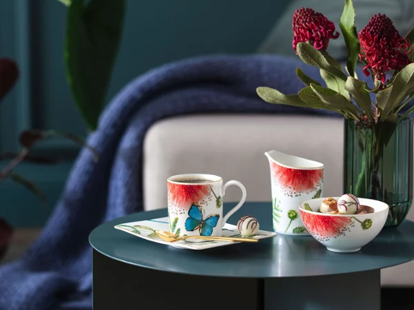 Table avec vaisselle Villeroy & Boch de la collection Amazonia Table avec vaisselle Villeroy & Boch de la collection Amazonia, dont une tasse, un pot et un bol, décorés de papillons et de fleurs. En arrière-plan, un bouquet de fleurs et une couverture.