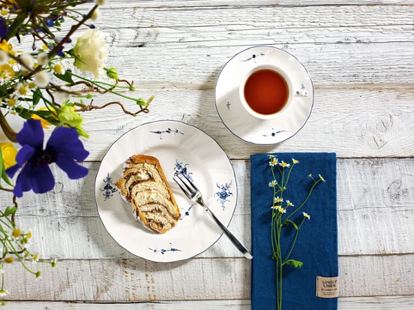 Une tasse à thé Vieux Luxembourg avec des pâtisseries sur une assiette. Une tasse à thé Vieux Luxembourg avec des pâtisseries sur une assiette, un livre et une composition florale sur une table en bois rustique.
