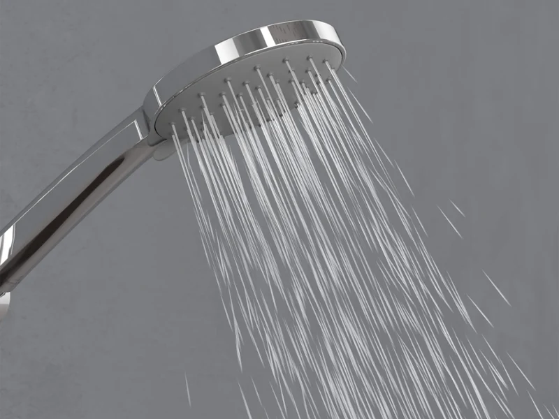 Douchette Universal Showers en mode Massage Un pommeau de douche chromé diffusant de légers jets d’eau vers le bas devant un simple fond gris.