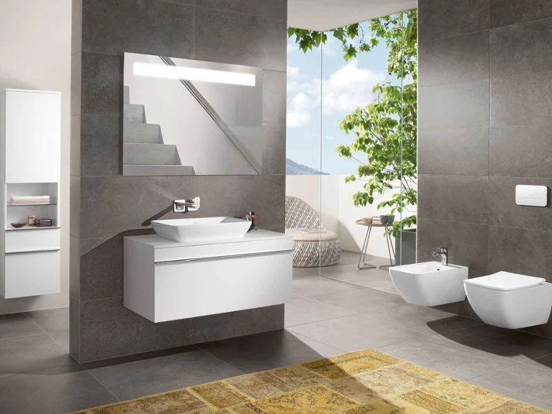 Un lavabo Venticello avec un miroir, un bidet et des WC Une salle de bains moderne avec un lavabo Venticello mural, un grand miroir, un bidet et des toilettes. Une fenêtre offre une vue sur la verdure et il y a un meuble blanc.