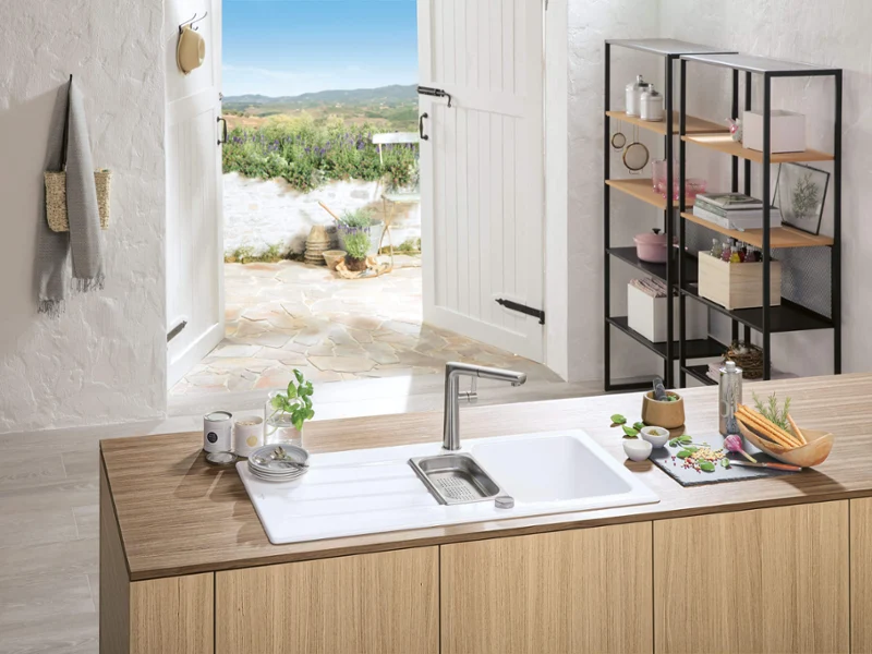 Un évier en céramique blanc Architectura avec une robinetterie Sorano Sky Shower Un évier blanc Architectura avec une robinetterie Sorano dans une atmosphère estivale avec un paysage de plage en arrière-plan