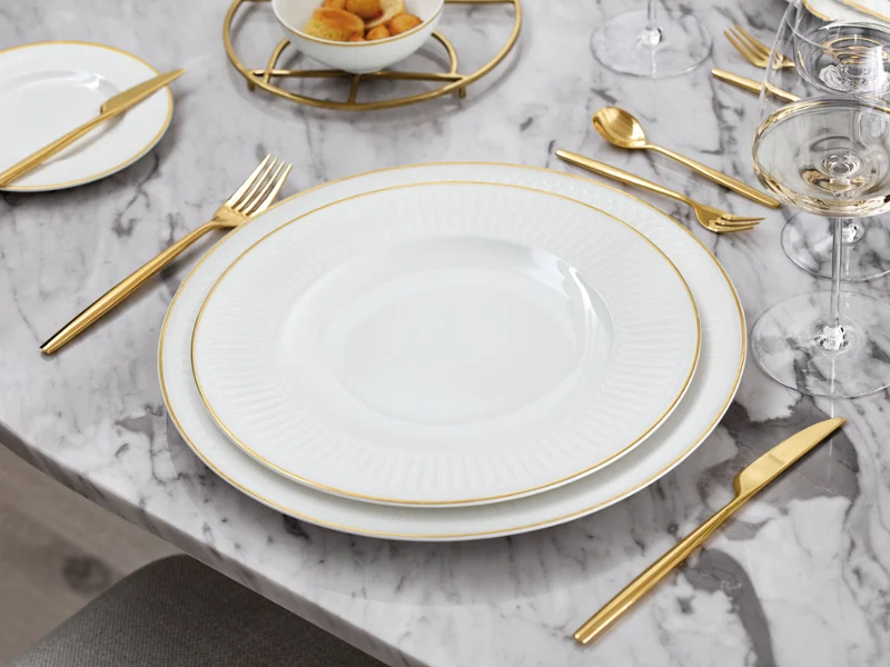 La collection Château Septfontaines dressée sur une table en marbre Un ensemble de vaisselle blanc et doré de Château Septfontaines sur une table en marbre.