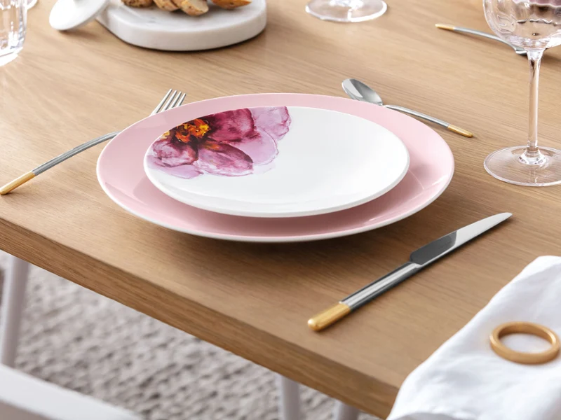 Une table dressée avec des assiettes Rose Garden et des couverts de table Ella aux notes dorées Une table de salle à manger minimaliste avec d’élégantes assiettes Rose Garden à motif floral, complétées par des couverts de table Ella modernes et dorés.