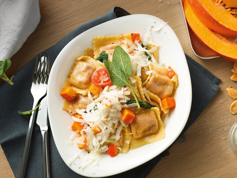 Une assiette de tortellinis Vapiano sur une table en bois avec des couverts de table Une assiette Vapiano avec des tortellinis sur une table en bois, avec des couverts de table Villeroy & Boch, une serviette et des tranches de citrouille