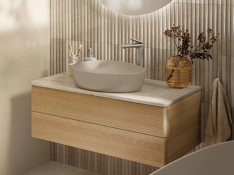 Des WC suspendus dans une salle de bains dans le style All Beige entièrement beige Des WC Subway 3.0 montés au mur avec Universo TwistFlush de Villeroy & Boch dans une salle de bains beige avec des rideaux transparents et une petite fenêtre.