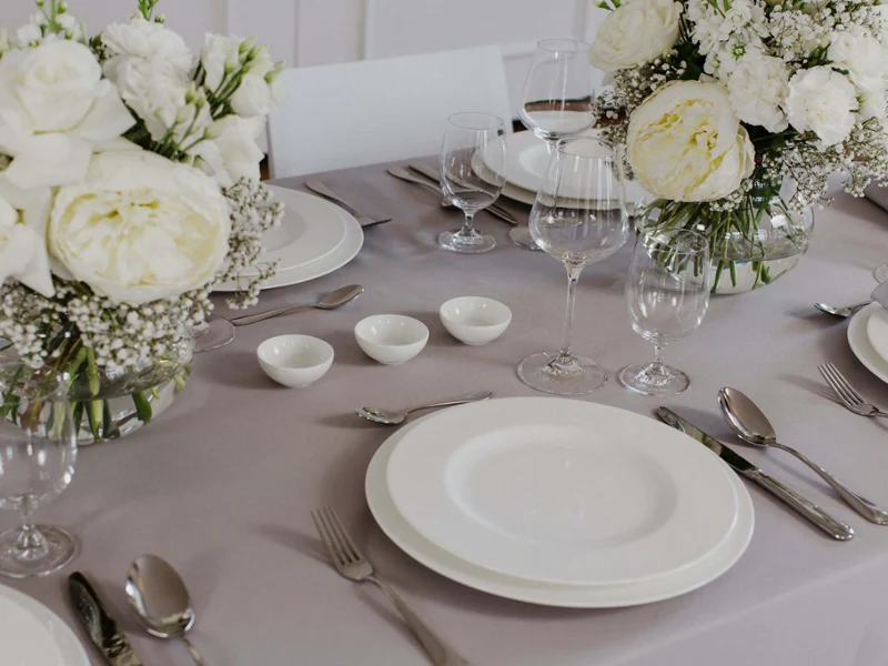 Des assiettes plates Royal avec une décoration florale Une table dressée avec des assiettes Royal ornées de compositions florales blanches pour une occasion formelle.