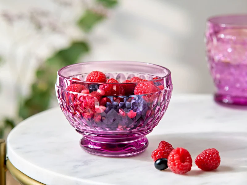 Un verre Boston violet contenant un mélange de bais est posé sur une table en marbre blanc. À côté, il y a quelques framboises et myrtilles. 