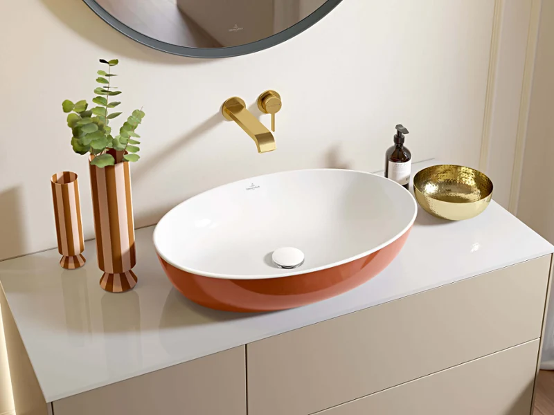 Un lavabo Artis couleur Rust dans une salle de bains moderne Un lavabo moderne orange et blanc dans une salle de bains avec des robinetteries dorées et des accessoires décoratifs