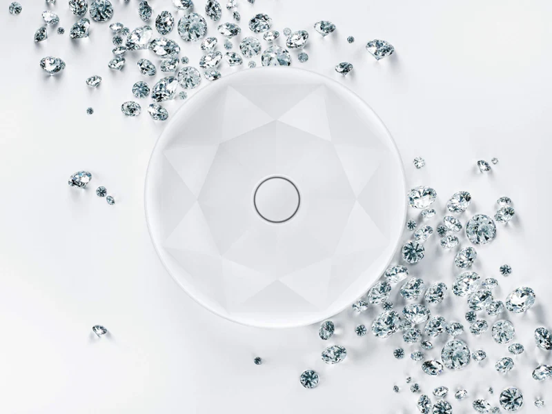 Un lavabo rond blanc aux motifs géométriques est entouré de petites et grandes pierres précieuses claires et facettées éparpillées sur un fond blanc.