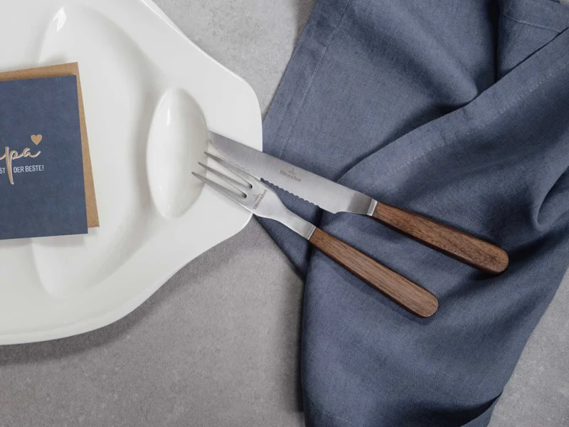 Des couverts de table Texas avec une serviette en lin Une décoration de table élégante avec des couverts de table Texas modernes avec des manches en bois et un menu posé sur une serviette en lin texturé.