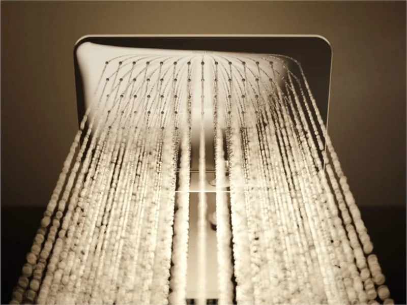 Un système de douche moderne Universal Shower avec une pomme de douche chromée Un espace de douche moderne dans la salle de bains avec des murs carrelés en noir, une pomme de douche chromée et une douchette à main. Un mur avec une structure en marbre entoure une fenêtre à droite et à gauche se trouve une niche avec des articles de toilette.