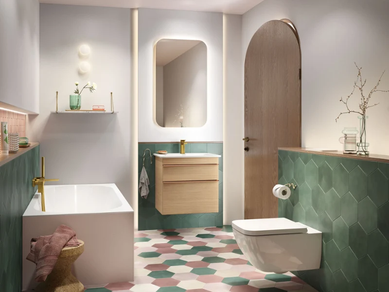 Une salle de bains Venticello avec baignoire, lavabo et toilettes Une salle de bains moderne avec une baignoire, un lavabo mural avec un miroir et des toilettes murales. La pièce est équipée de carreaux de sol hexagonaux dans les couleurs vert, rose et blanc.