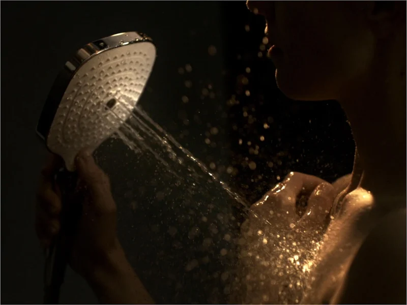 Un système de douche moderne Infinity Shower avec une douche de tête carrée Un système de douche moderne avec une pomme de douche carrée, une pomme de douchette à main fixé sur une barre et un robinet de commande thermostatique montée sur un mur avec une surface marron structurée.