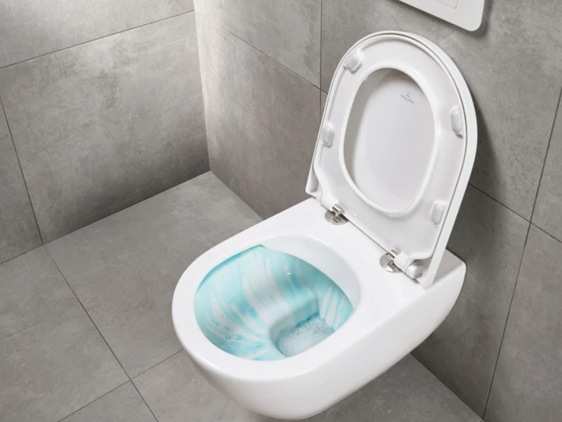 Des WC muraux blancs Des toilettes murales avec technologie Flush de Villeroy & Boch, sur fond de carrelage gris. Le couvercle des toilettes est ouvert et laisse entrevoir la cuvette qui contient une solution de nettoyage.